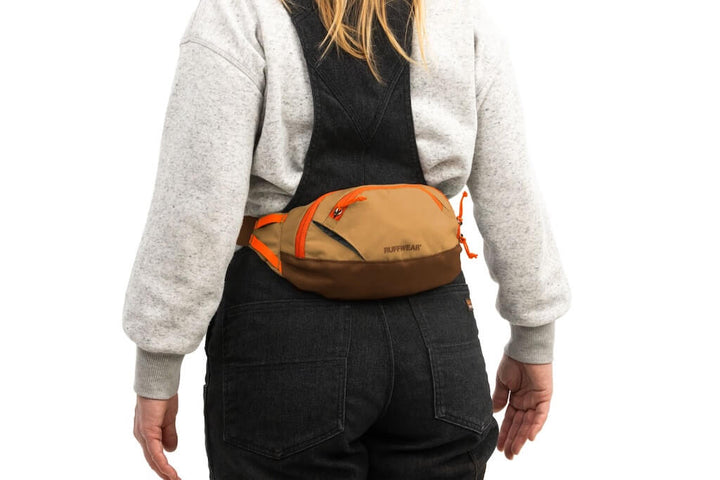 Person wearing a Ruffwear Home Trail Hip Pack - a brown waist bag with orange accents on a white background