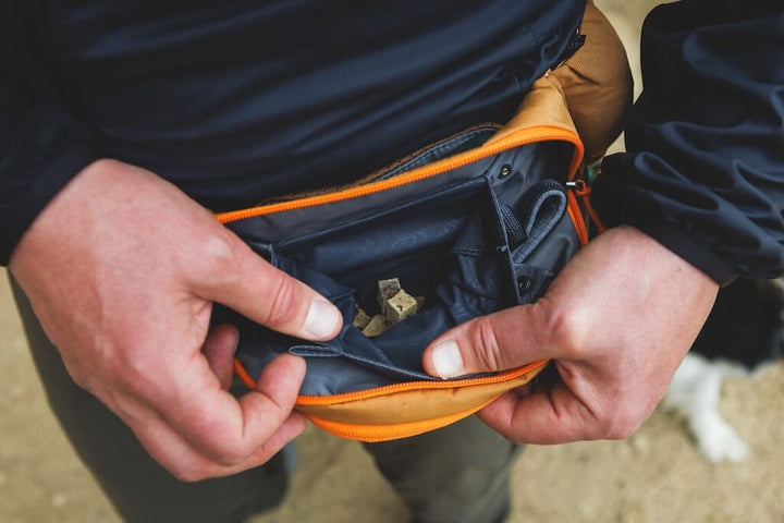 Person opening a one of the zippers of the Ruffwear Home Trail Hip Packs showing where kibble can be kept.  
